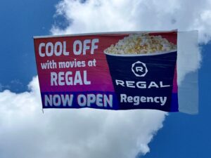 Brightly colored aerial billboard flying through the blue skies, featuring an image of a bucket of popcorn to advertise a Regal Cinemas movie theater.